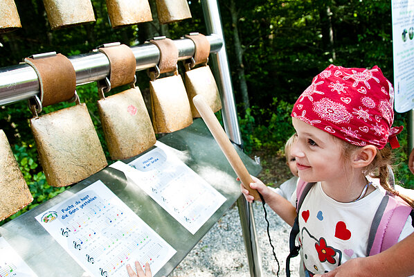 Junges Mädchen spielt auf dem Kuhglockenspiel am Pfaffenwinkler Milchweg.