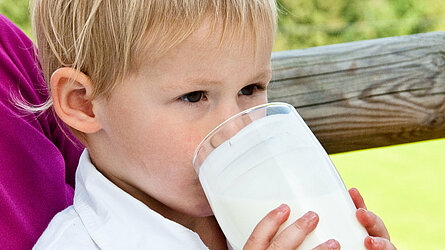 Junger Bub trinkt aus einem Milchglas.